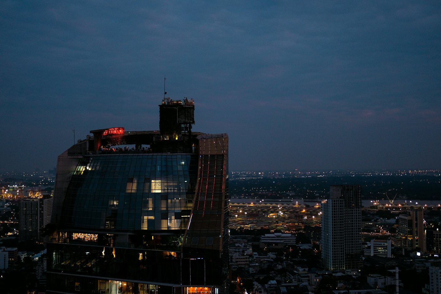 People enjoying a rooftop bar in a modern skyscraper at dusk.